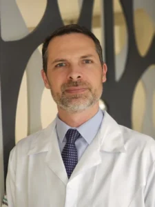 Foto do Dr. Phillipe Heckler, Médico Urologista, de jaleco branco e gravata azul.