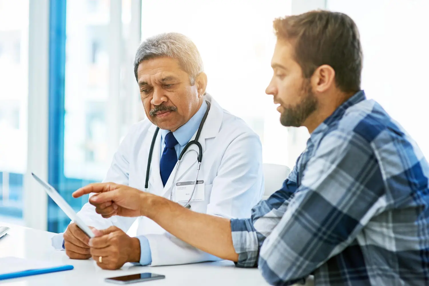 Homem de camisa xadrez conversa com um médico para esclarecer dúvidas, representando a pergunta: “posso fazer vasectomia sem ter filhos?”